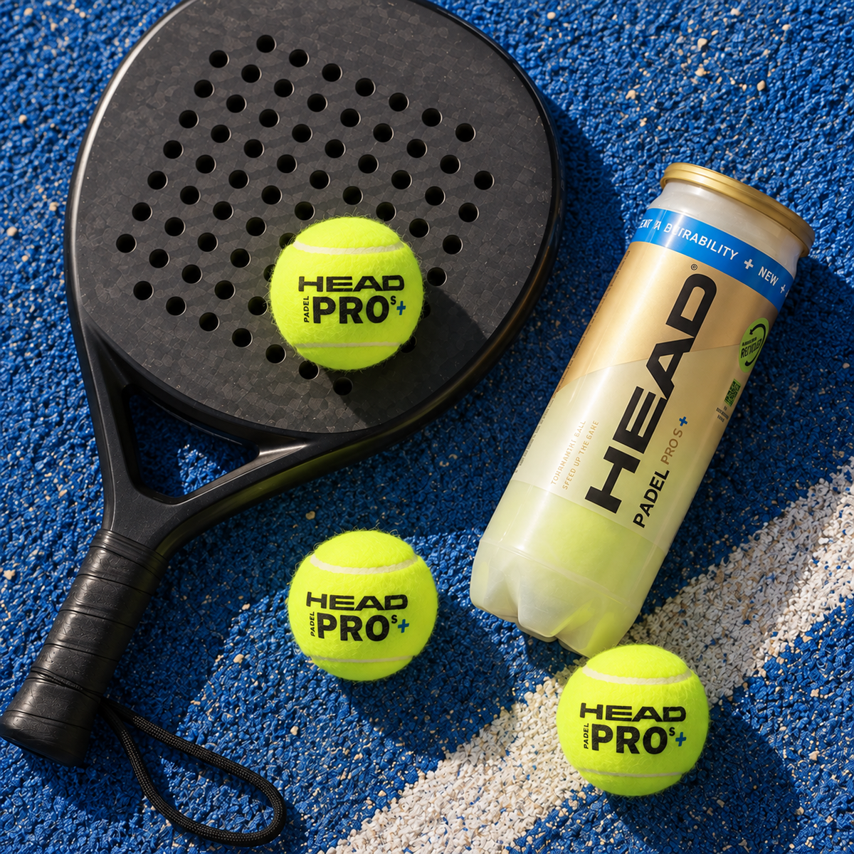 Flat lay of a black carbon padel racket, three HEAD Padel Pro S+ balls and a tube of balls on a blue padel court.